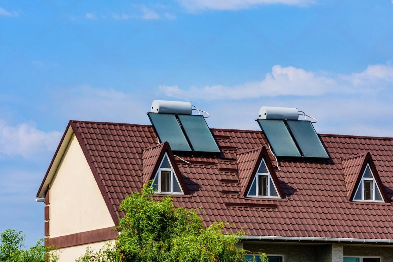 Rooftop solar water heaters on a house with red tiled roof under a blue UAE sky