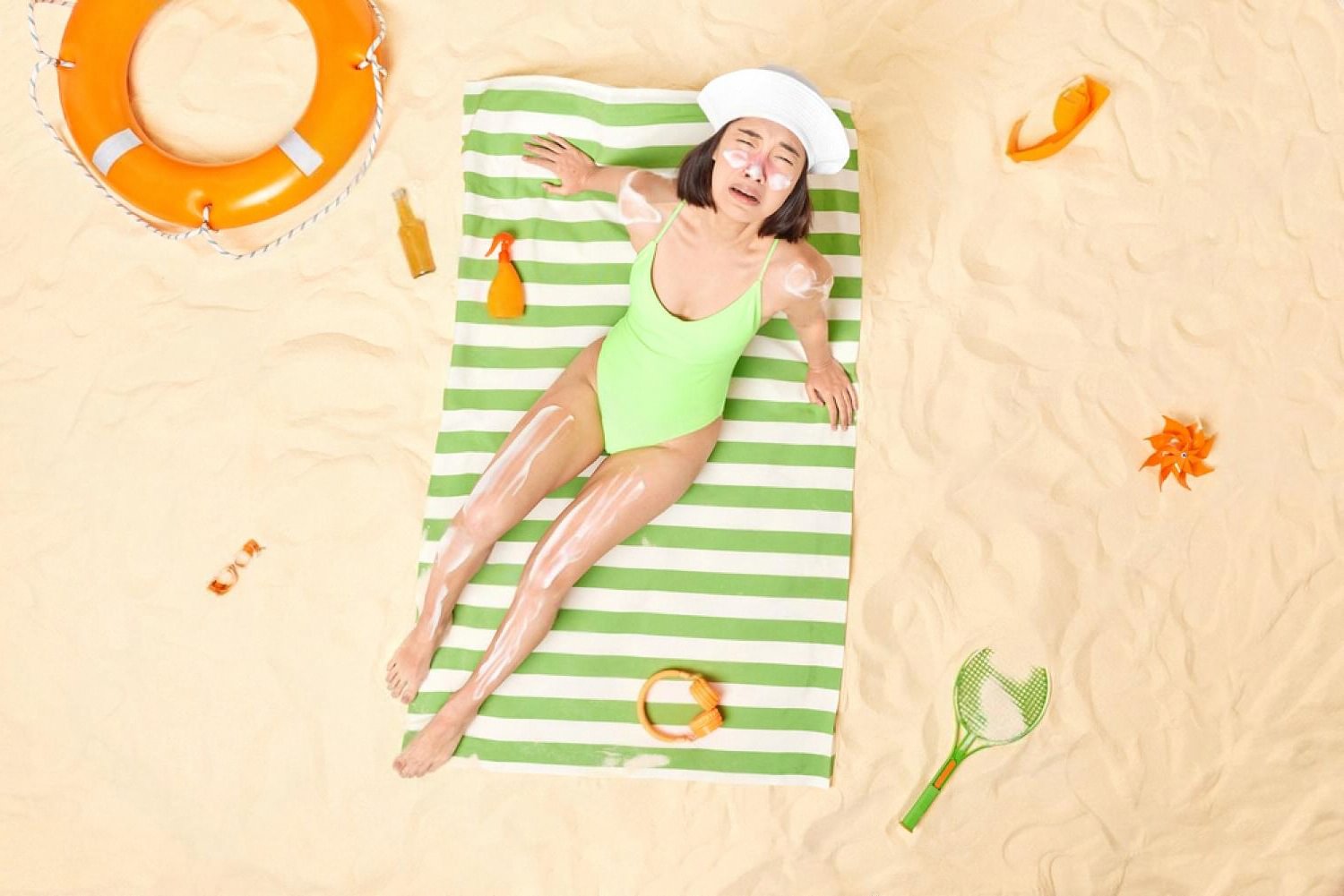 Woman with sunburn and peeling skin lying on a beach towel under strong summer sun